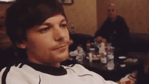 a man is sitting at a table in a room with a man sitting behind him .