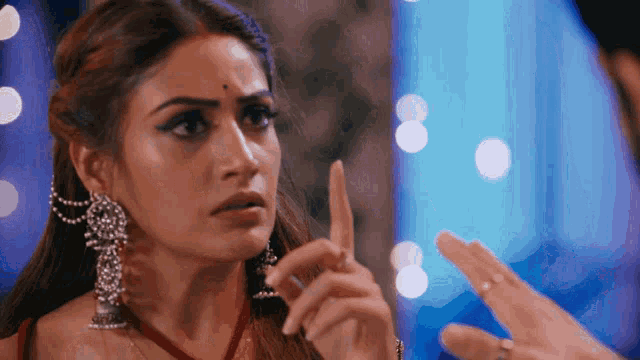 a woman wearing earrings and a red necklace points her finger at someone