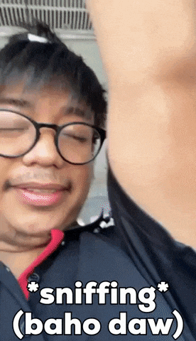 a man wearing glasses is sniffing his armpit and the caption says sniffing ( baho daw )