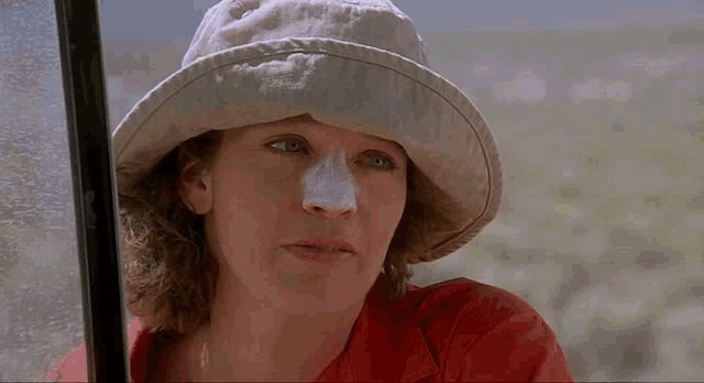 a woman wearing a hat and a red shirt has a white patch on her nose