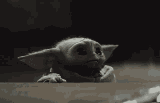 a baby yoda looking over a table with a serious look on his face