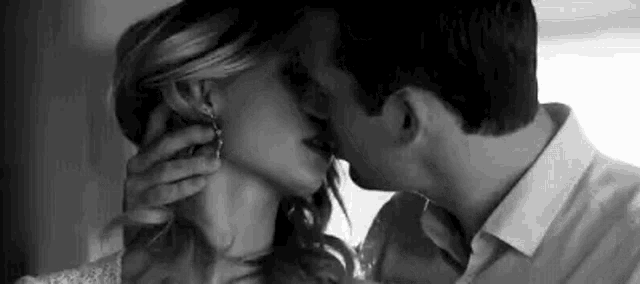 a black and white photo of a man and a woman kissing .