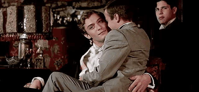 a man in a suit is holding another man in his arms in a room .