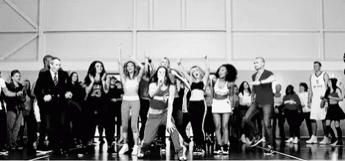 a black and white photo of a group of people dancing on a basketball court .