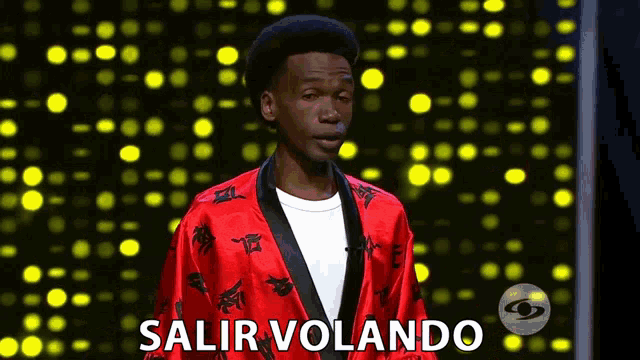 a man in a red robe is standing in front of a yellow background and says salir volando .