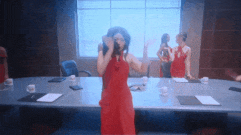 a woman in a red dress stands at a conference table