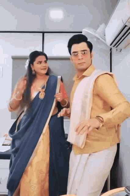 a man in a yellow shirt is standing next to a woman in a blue saree