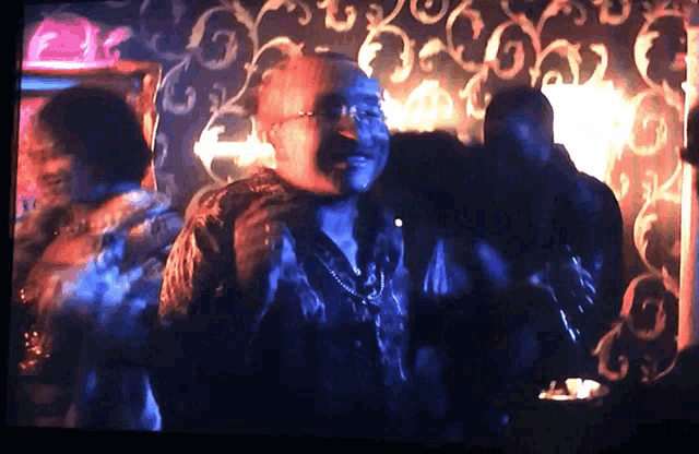 a man with glasses is dancing in a dark room with a patterned wallpaper