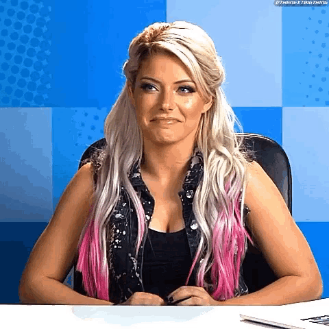 a woman with blonde hair and pink streaks is sitting at a table with a laptop .