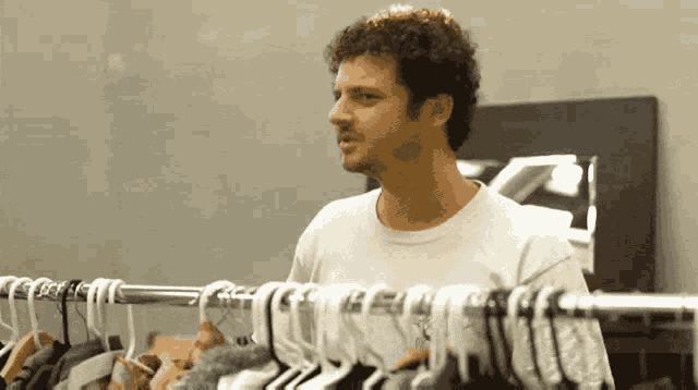 a man in a white shirt is standing in front of a rack of clothes with a few hanging on it