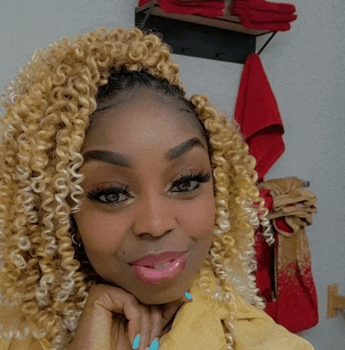 a woman with blonde curly hair and blue nails looks at the camera