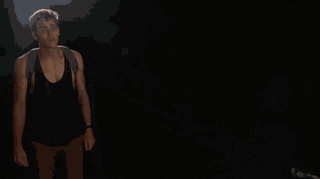 a man with a backpack is standing in the dark .