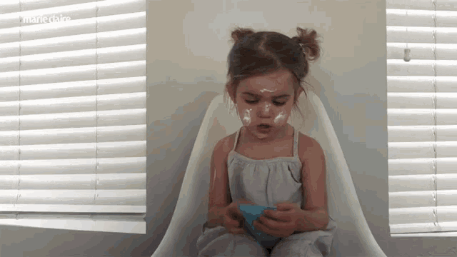 a little girl is sitting in a chair with a bowl of food on her face and the words mangedaire on the bottom
