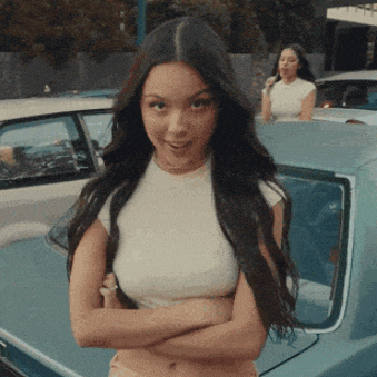 a woman is standing in front of a car with her arms crossed and smiling .