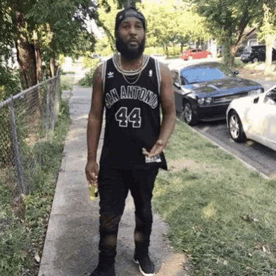 a man wearing a black san antonio jersey is standing on a sidewalk