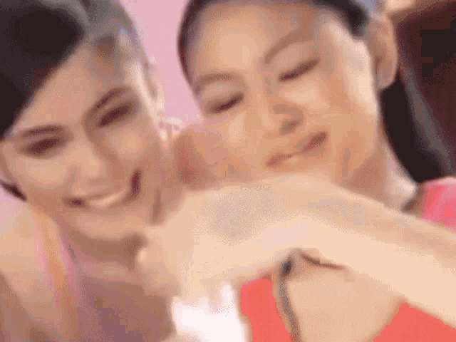 two women are smiling and hugging each other in a pink room .