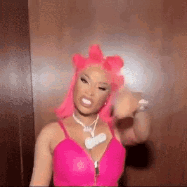 a woman with pink hair and a pink top is standing in front of a wall .