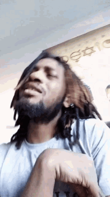 a man with dreadlocks and a beard is sitting in front of a sign that says ' design ' on it