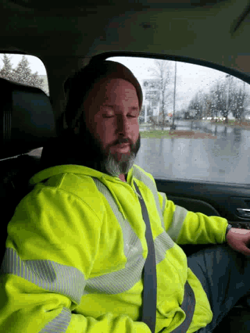 a man with a beard wearing a yellow safety vest is sleeping in a car
