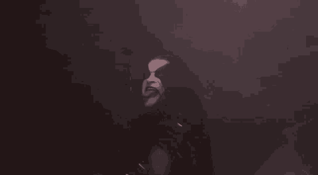 a man with a black mask on his face is standing in the dark with his tongue out .