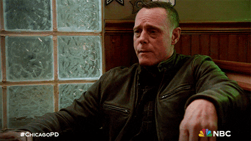 a man in a leather jacket sits in front of a glass wall with the nbc logo on the bottom right