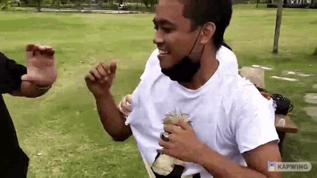 a man wearing a mask and a white t-shirt is standing in a park .