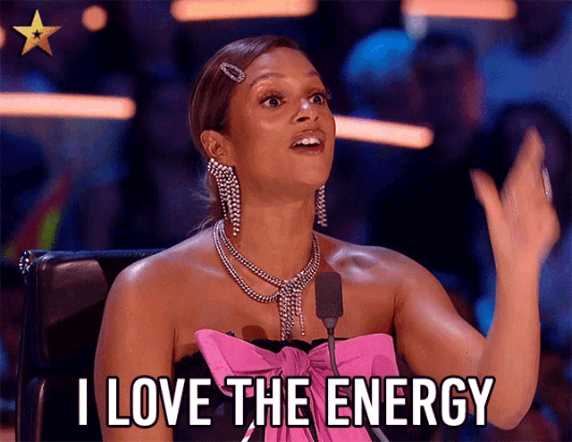 a woman in a pink bow dress says i love the energy in front of a microphone