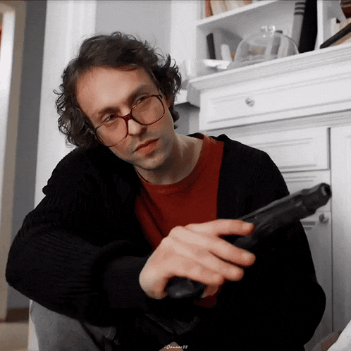 a man wearing glasses holds a gun in his hand