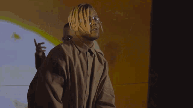 a man with dreadlocks and glasses is standing in front of a wall