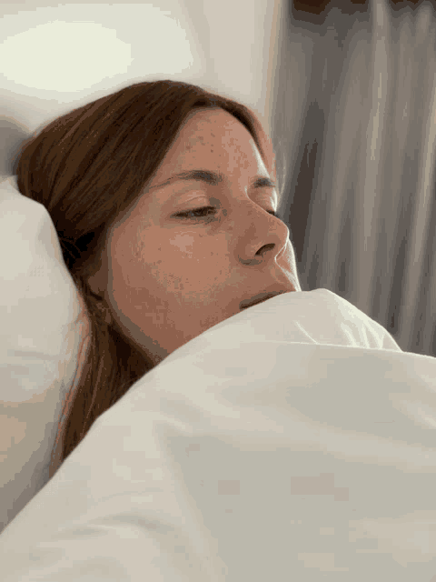 a woman with freckles is sleeping in a bed with white sheets