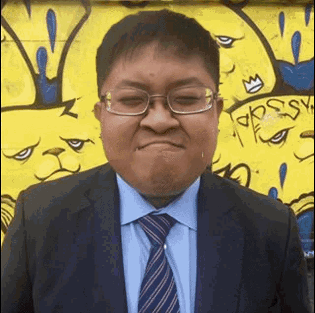 a man in a suit and tie is making a funny face in front of a yellow wall .