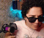 a woman wearing sunglasses and a necklace is holding a camera .