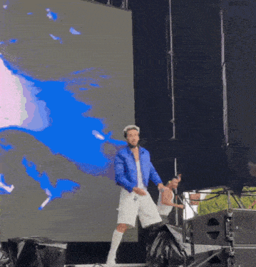 a man in a blue jacket and white shorts is dancing on a stage .