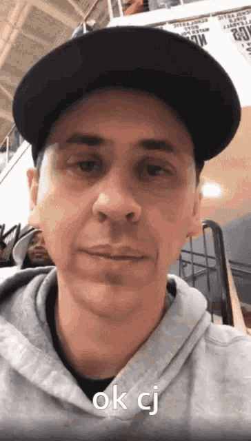 a man wearing a black hat and a grey hoodie says ok cj on his face