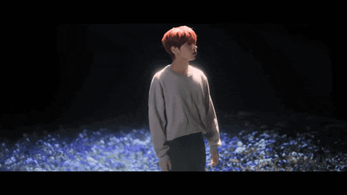 a young man with red hair is standing in a field of flowers