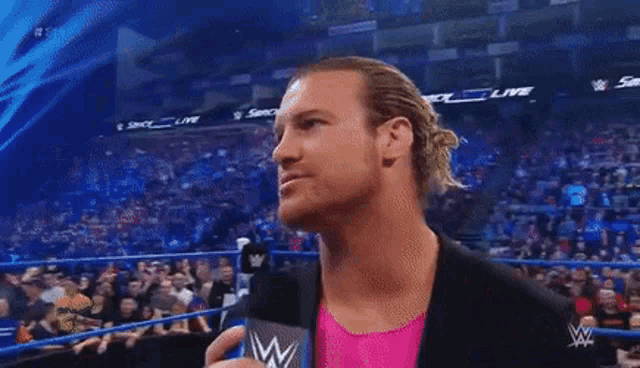 a man in a pink shirt is talking into a microphone while standing in front of a crowd .