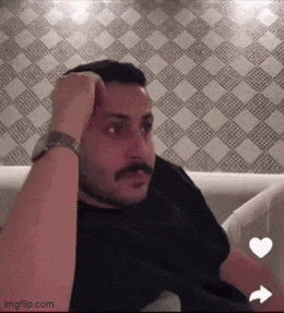 a man with a beard is sitting on a couch with his hand on his head .