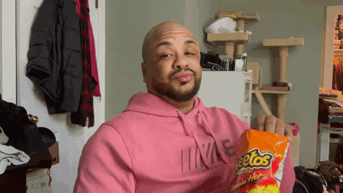 a man in a pink hoodie holds a bag of cheetos chips