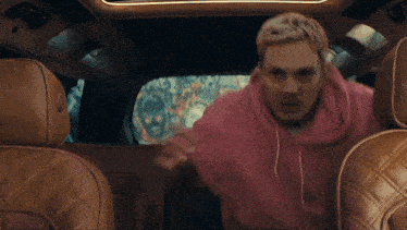 a man in a pink shirt is sitting in the back seat of a car and says " did "