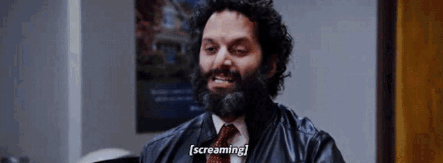 a man with a beard and tie is screaming while wearing a leather jacket .