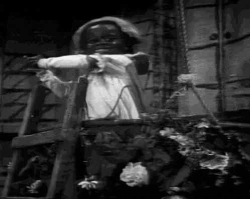 a black and white photo of a little girl standing on a ladder next to a basket of flowers .