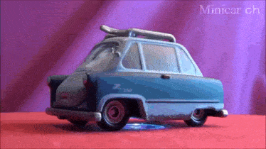 a blue toy car with a surfboard on the roof is sitting on a red surface with the words minicar ch visible in the corner