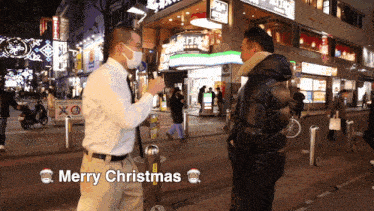 a man wearing a face mask is talking to another man on a street and the words merry christmas are displayed