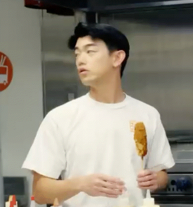 a man in a white shirt is holding a hot dog on a stick .