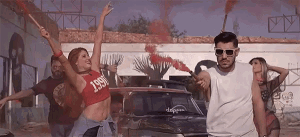 a man and a woman are dancing in front of a car with smoke coming out of the window .