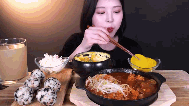 a woman is eating a bowl of food with chopsticks while sitting at a table