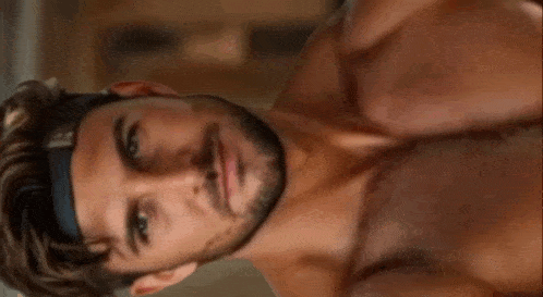 a shirtless man with a beard and a headband on his head is looking at the camera .