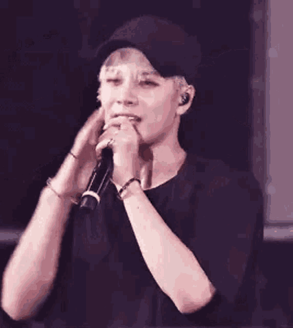 a man is singing into a microphone while wearing a hat and waving his hands .