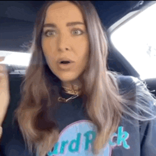 a woman wearing a hard rock sweatshirt is sitting in a car with her mouth open .