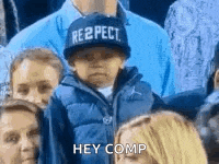 a boy wearing a hat that says respect is sitting in a crowd of people .